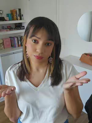 A woman with brown hair and bangs is in a room with a white wall and white furniture. She is wearing a white v-neck shirt with heart-shaped earrings and her hands are open in front of her body as if making a point. There is text overlay over the images.