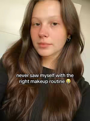 A young woman with long brown hair looks directly at the camera in a medium shot. The text overlay says, "never saw myself with the right makeup routine". The background is a simple, plain white wall.