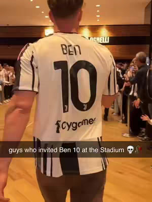 A person from the back wearing a Juvents jersey, and the number 10 is visible. Text overlay shows a text against the jersey. People in background are on the sides. Flooring suggests a stadium like location.