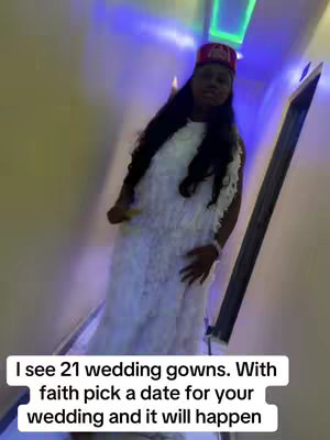 A woman wearing a white, textured dress stands in a well-lit hallway. She's wearing a red and gold head covering. The background has a light blue color and the text overlay is on the bottom of the image.