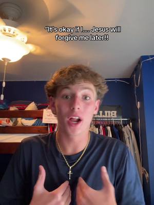 A young man with short brown hair and a navy blue shirt speaks into the camera with an energetic expression, gesturing with both hands. He is wearing a gold chain with a cross pendant. The background features a room with blue walls, a chandelier, and a clothing rack.