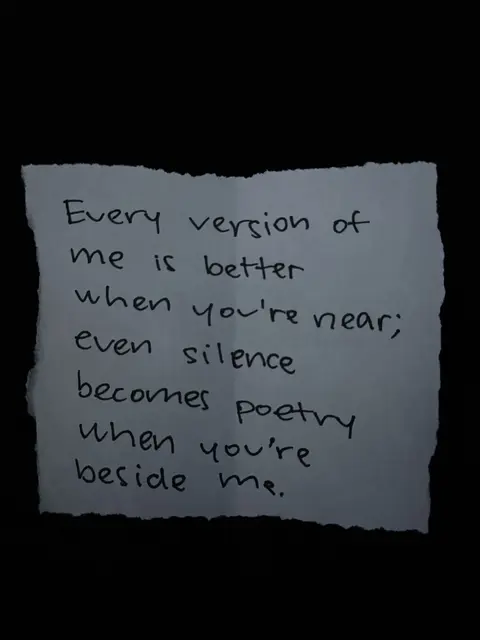 A close-up shot on a piece of torn paper against a dark background. The paper has handwritten text in black ink. The text is a quote of love. The background is solid black.