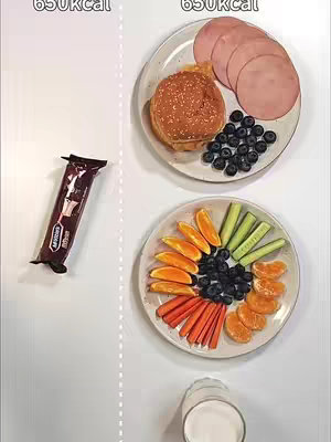 An overhead shot displays two plates of food, representing a comparison. On the left, a wrapped chocolate bar is isolated. On the right, one plate holds a hamburger, sliced ham, and blueberries, while the other has orange slices, cucumber slices, carrots, blueberries, and mandarin orange slices. Text overlays label the calorie counts for each food group.