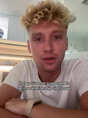 A close-up shot of a young man with spiky blonde hair and a white t-shirt, lit by soft indoor lighting. He is looking at the camera and appears to be speaking. Text is overlaid at the bottom.