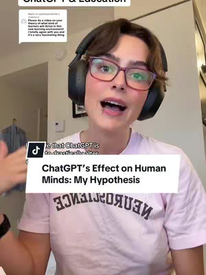 A person with short dark hair and glasses wearing a light pink t-shirt is talking while looking at the camera. She has a headset on. A white rectangle overlay with black font appears to be in the bottom center of the video. The background consists of a wall, a door, and an article of clothing hanging on a hanger.