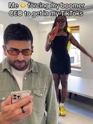 The cover image shows two people, one man in the foreground focused on a phone, and a woman in the background. The man is wearing a green button-up shirt and orange-tinted glasses, while the woman in a black dress is holding a bottle, with a gold foil balloon behind her. Text overlays the image, indicating the content is about forcing a CEO to participate in TikToks.