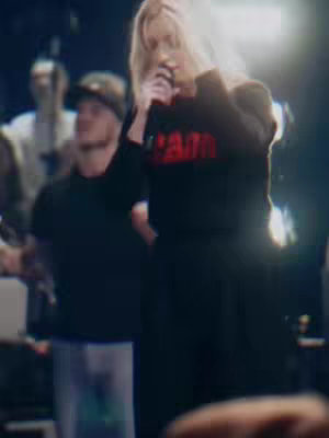 The cover image shows a woman on a stage, holding a microphone and singing. The background is dark, with other people blurred in the background. The woman is wearing a black top with the word "PAIN" in red letters.