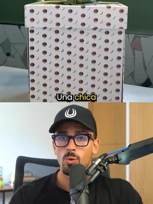 The image is split into two parts. The top half shows a large, decorative gift box covered in a pattern of dark red circles and crescent shapes over a white background. The bottom half features a man with glasses and a black hat talking into a microphone.