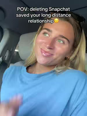 A woman is sitting in a car filming a selfie video. She has blonde hair, green eyes and is wearing a blue shirt. The background is a blurred car interior. Text overlay reads: POV: deleting Snapchat saved your long distance relationship.