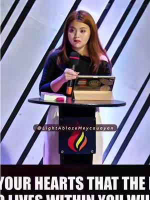 The image shows a woman giving a sermon. She is holding a microphone and has an expressive face. A podium and a backdrop of white and black lines complete the setting.