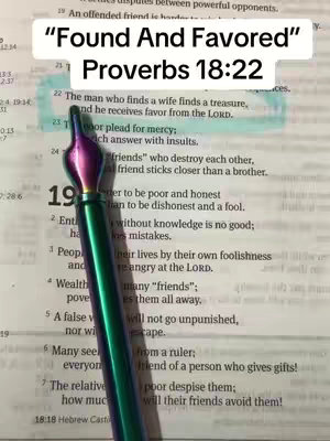 The image shows an open book with the text of Proverbs 18:22 highlighted. The words "Found and Favored" are written over the top in a large, white font. There is a decorative pen placed near the verse. The lighting is natural.