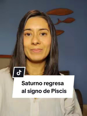 A woman with long dark hair is centered in the frame. Behind her is a blue wall with wooden fish decorations. A white banner with the text "Saturno regresa al signo de Piscis" is at the bottom. A TikTok logo is in the bottom left corner.