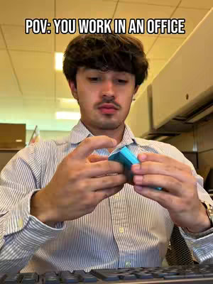 A man is shown in the office setting with a striped shirt, interacting with a small object in his hands. The background includes the office infrastructure, creating a work-related atmosphere.