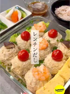 The image showcases a close-up view of homemade steamed dishes in a clear glass container, arranged on a white surface. The dishes are small, round portions filled with beige material, topped with bright red cherry tomatoes and small shrimp. Some also have shiitake mushrooms. Beside the main dish is a small bowl of clear sauce. The presentation suggests a healthy meal.