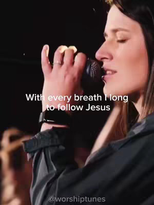 A woman with brown hair is pictured in profile, facing right and singing into a microphone. She is dressed in a dark long sleeve top against a blurred background. Text is overlaid on the image.