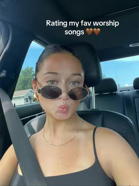 A woman wearing sunglasses pouts at the camera while sitting inside a car. Text overlays the top of the image. The lighting appears to be from the sun.