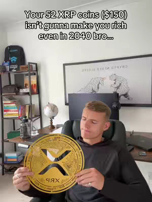 A man sits in front of a desk, holding a large, gold-colored XRP coin. Text overlayed above the man states that 52 XRP coins, valued at $150, won't make him rich by 2040. The man appears to be looking at the coin with a thoughtful expression, with a desk in the background.