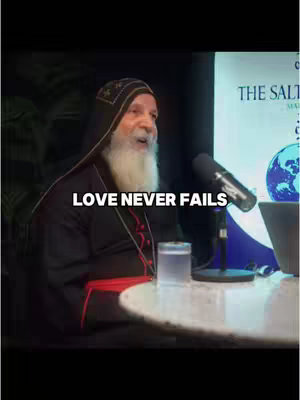 A man with a white beard and a dark robe is seated, and the text overlay states "LOVE NEVER FAILS."
