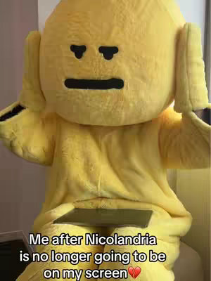 A person in a yellow costume with a large head and black eyes and mouth stands holding a device. Text overlayed on the image.
