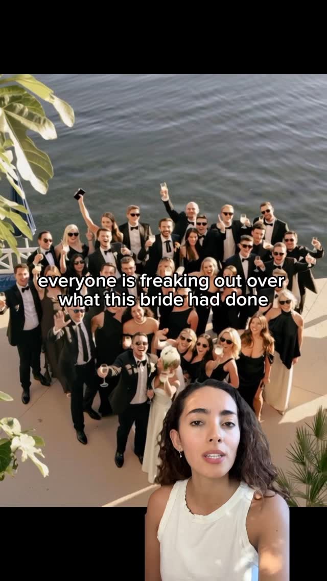 A photo features a diverse group of people in formal attire, possibly a wedding party, gathered on a deck overlooking a body of water. The composition is centered, with the group posing closely together, some raising glasses in a celebratory gesture. A woman is in the foreground in front of them, speaking to the audience. The overall lighting is bright, and the colors are natural, creating a sense of occasion and joy.