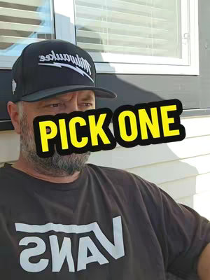 A man with a beard wearing a black cap and a Vans t-shirt is looking slightly to his left. A bright yellow and black overlay says 'PICK ONE'.