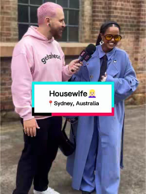A man with pink hair interviews a woman wearing sunglasses and a blue coat; text overlay reads "Housewife" and "Sydney, Australia."