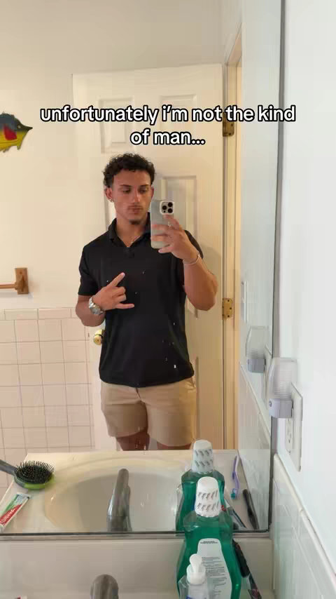 A man is shown in a bathroom, holding his phone up to record a selfie. The background includes a mirror, sink, and bathroom fixtures. The hook overlay reads: 'unfortunately I'm not the kind of man...'