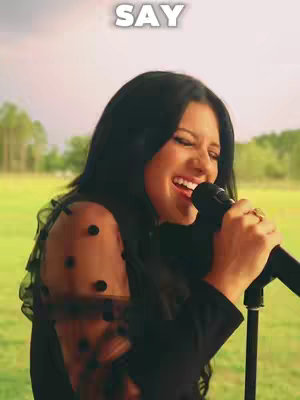 The cover image shows a woman singing into a microphone on a stage, with a blurred natural background. The woman is wearing a black outfit with sheer, dotted sleeves and a gold ring. She's smiling and appears to be mid-performance near a microphone stand.