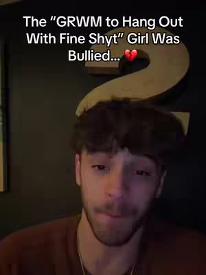 The cover image features a close-up of a young man with short, dark, tousled hair, looking slightly to the side. He has a light complexion and a hint of a smile or smirk. Above the man, the text is placed, it reads 'The "GRWM to Hang Out With Fine Shyt" Girl Was Bullied...'. In the background, there's a dark, slightly out-of-focus area that suggests a room setting, possibly a bar or a dimly lit space, with a large decoration behind him. His attire appears to be a brown sweater or shirt, making it a simple and straightforward composition.