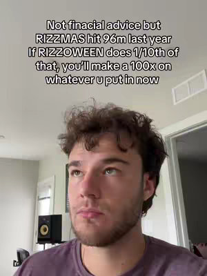 A selfie-style shot featuring a young man with short, curly brown hair, gazing upward with a thoughtful expression. The man is wearing a purple t-shirt. The background is a room with white walls and a window and a speaker.