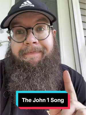 A man with a beard and glasses is pointing his index finger upward. He is wearing a black Adidas cap and a black shirt. A text overlay at the bottom reads 'The John 1 Song.'
