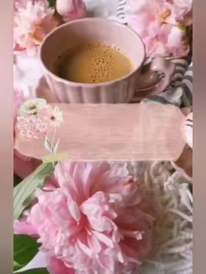 A close-up shot of a light pink teacup with coffee, surrounded by pink flowers. There is a light-pink text box over a floral arrangement. 