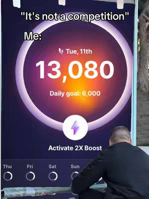 The cover image shows a man looking down at a large display screen showing a fitness app interface. The screen displays a circular graphic with the user's step count (13,080) and daily goal (6,000), along with the weekday. Text overlays, including a playful phrase like "It's not a competition", appear at the top. The overall composition uses a limited color palette, focusing on purple, white, and a hint of orange, with a figure of a man partially visible. The man is dressed in dark clothing, adding to the minimalist style.