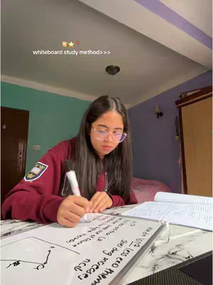A woman with long dark hair and glasses is writing on a whiteboard in a room with a blue and purple wall. She is wearing a maroon shirt and a pen is in her hand. There's a book on the table next to the whiteboard. The text overlay highlights the study method.