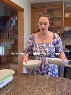 A woman is in a kitchen holding two white bowls. She's wearing a blue and white patterned dress and has her hair pulled back. The kitchen has light-colored cabinets and a staircase is visible in the background. Text that says 'Yesterday, I filed for divorce' is overlaid on the image.