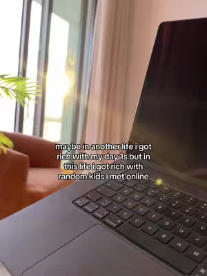 The photo shows a laptop on a table, with the screen angled towards the viewer, showing the keyboard. In the background, there is a blurred setting with a window letting in some sunlight.
