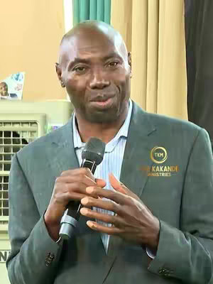 A man in a suit holding a microphone, he seems to be in a service to deliver a sermon.