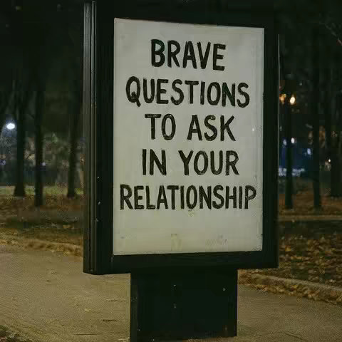 A nighttime shot of a street sign with black lettering that reads, 'BRAVE QUESTIONS TO ASK IN YOUR RELATIONSHIP,' set against a background of trees and streetlights. The sign is in a metal frame on top of a black rectangular base, with a slightly blurred, dark, natural nighttime atmosphere.