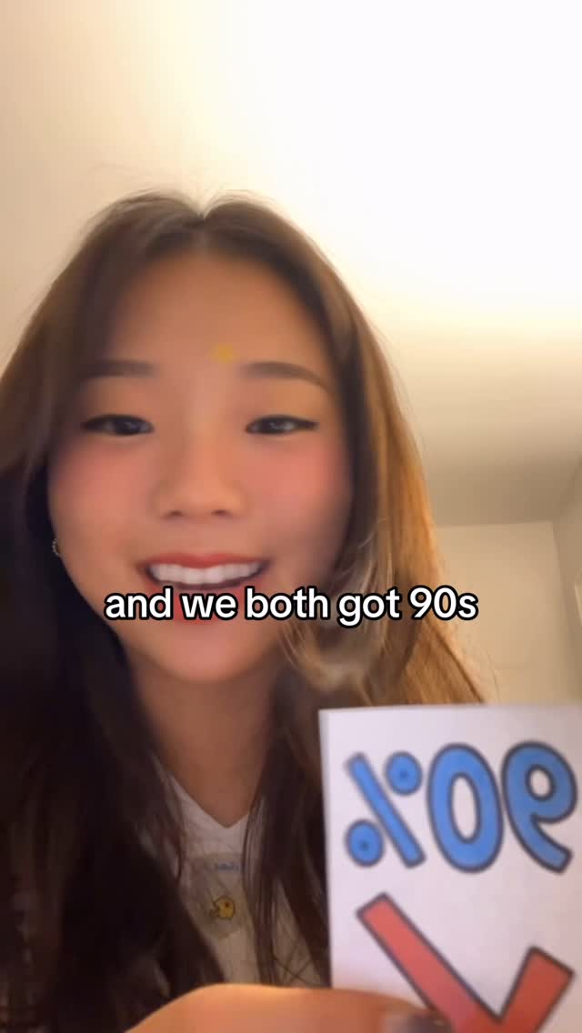 The cover image features a close-up shot of a young woman with long, brown hair. She is smiling and holding a card that has a partially visible design, with text overlayed at the bottom reading "and we both got 90s". The background appears to be a plain wall.