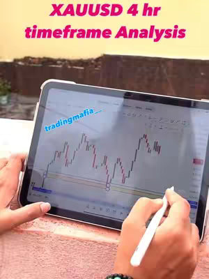 A person is holding a tablet displaying a stock chart and using a stylus to analyze it. The tablet screen shows red and white candlestick charts indicating market fluctuations. The background is a blurred outdoor setting, possibly a rooftop.