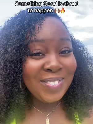 A close-up shot of a smiling Black woman with curly hair. She has a necklace and the background is blurred.