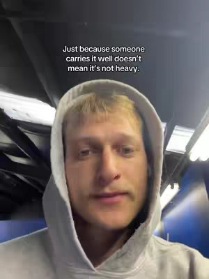 A man in a gray hoodie looks directly at the camera in what appears to be a casual setting, with text overlayed at the top.