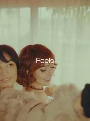 The cover image shows a soft-focus shot of a group of young women, partially obscured, in a party setting. The word "Feels" in a clean white font overlays the image near the top center.