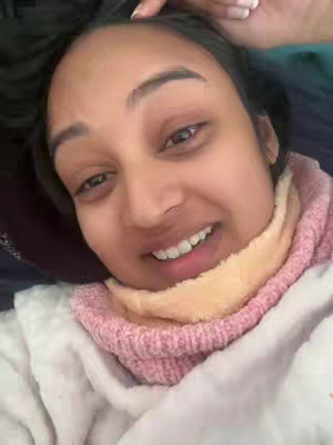 The cover image shows a close-up selfie of a woman lying down. She has dark hair and is smiling, revealing her teeth. She is wearing a pink and tan scarf and a white top, and her arm and hand are seen at the top left of the frame. The lighting appears to be soft and natural.