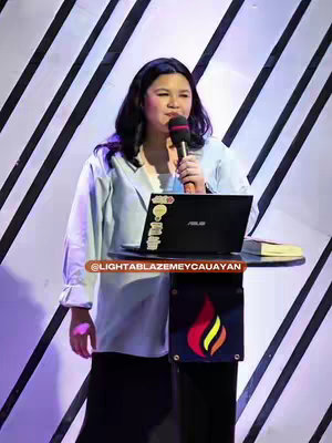 The cover image features a woman speaking into a microphone while positioned behind a podium. The podium is partially adorned with a colorful logo. Behind her is a background with vertical stripes. The colors are a mix of pale blues, dark navy, and white. There is a laptop on the podium.