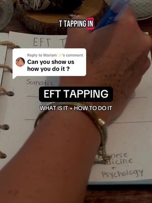 The image captures a close-up view of a person's hand writing or drawing on a sheet of paper. The person's arm is visible with a bracelet. Text overlayed on the image says "T TAPPING IN" and "EFT TAPPING WHAT IS IT + HOW TO DO IT". A bubble from instagram comments on the upper left displays a comment. A handwritten note is visible, with some labeled text, providing a visual guide.