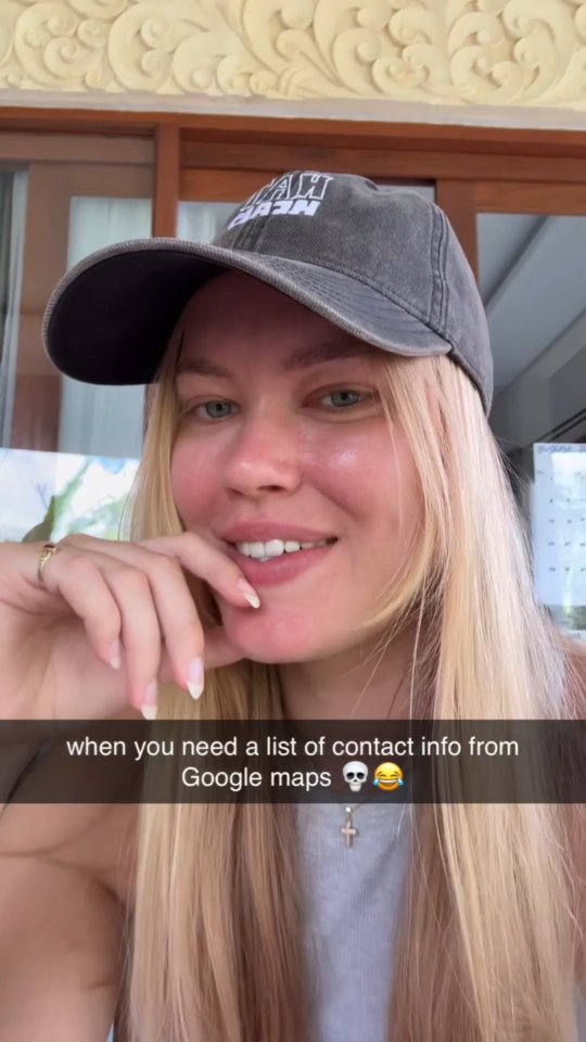 A selfie-style shot features a fair-skinned woman with blonde hair and a gray cap. She smiles gently while touching her face with one hand, and text overlaid on the image reads, 'when you need a list of contact info from Google maps' with a skull and laughing emoji.