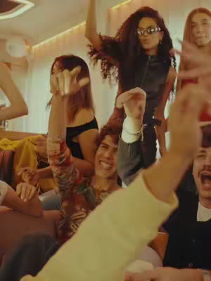 A group of young people are gathered in a lively and energetic setting, raising their arms in excitement. The individuals are diverse in appearance and are dressed in casual, stylish attire. The image is filled with a sense of joy and communal atmosphere, reflecting a vibrant social event. The color palette is warm and inviting, with the focus on the group’s enthusiasm. The composition is dynamic, inviting the viewer to feel the collective energy of the moment.
