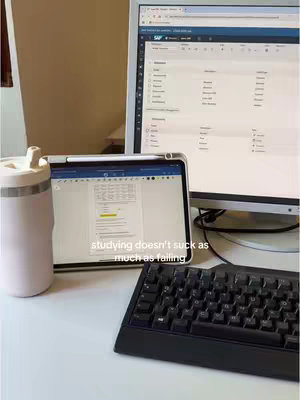 The image shows a workspace setup with a tablet, a computer monitor, a keyboard, and a water bottle. On the tablet screen, a document is displayed, and the text overlay says 'studying doesn't suck as much as failing.'