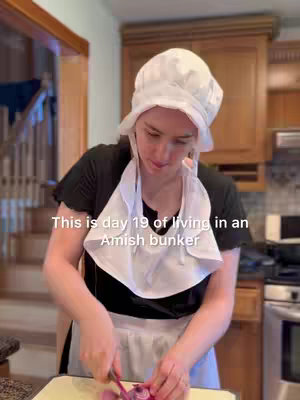 A woman in a white bonnet and apron stands in a kitchen, preparing food and cutting vegetables. Text overlaid indicates this is day 19 of living in an Amish bunker.